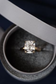 an engagement ring in a box with a white ribbon around it and a cushion cut diamond