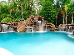 a large pool with waterfall and rocks in the middle, surrounded by greenery on both sides