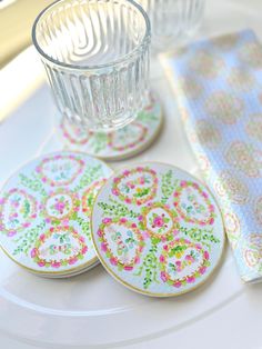 four coasters with colorful designs on them sitting on a plate next to a glass