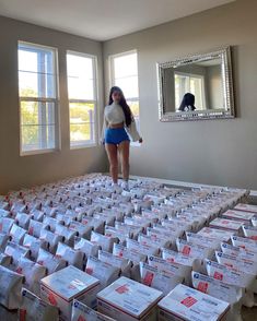 a woman standing in the middle of a room filled with boxes and packages on top of it