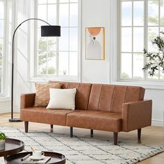 a brown leather couch sitting on top of a white rug in a living room next to two windows