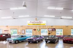 several classic cars are parked in a large room with wood paneling on the walls