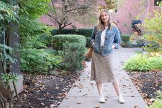 a woman standing on a sidewalk in front of some trees