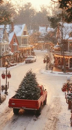 a red truck carrying a christmas tree down a snow covered street in front of houses