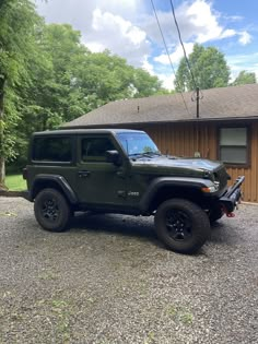 a black jeep parked in front of a brown house with trees and grass around it