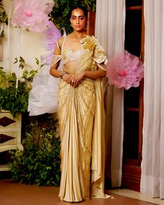 The flower patch on the shoulder seems like it is blooming from the joy of the season. The draped saree made with lightweight fabric materializes the concept of a fairy. The gold saree is embellished with beadwork and applique flowers all around to appear as if standing amongst flowers. Cold shoulder style blouse with back hook Pre-draped saree with a flower patch on the shoulder accentuated with beads and sequins embroidery. Metal zip on the saree. From Moledro’s Taabir collection. DELIVERY TIM Festive Gold Embellished Pre-draped Saree, Gold Pre-draped Saree With Sheer Dupatta For Navratri, Gold Pre-draped Saree With Gota Work For Wedding, Gold Pre-draped Saree With Resham Embroidery For Reception, Traditional Pre-draped Tissue Silk Saree With Dupatta, Gold Raw Silk Pre-draped Saree For Festivals, Festive Gold Art Silk Pre-draped Saree, Bollywood Style Pre-draped Saree In Raw Silk, Festive Pre-draped Saree With Gota Work