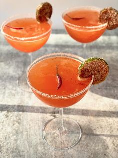 three glasses filled with drinks sitting on top of a table