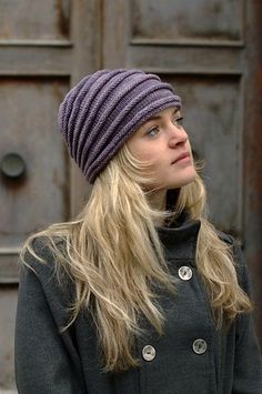 a woman wearing a purple hat standing in front of a wooden door and looking off into the distance