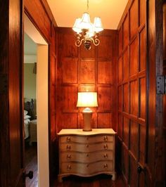 a room with wood paneling and a lamp on the dresser in it's corner