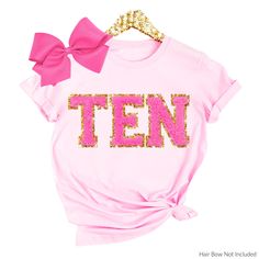 a pink tee shirt with the word ten printed on it and a bow at the front