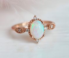 an opal and diamond ring on a white surface with pink feathers in the background