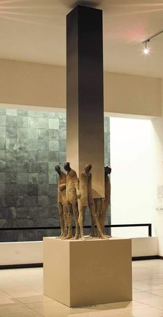 three statues on pedestals in an empty room with tile flooring and walls behind them