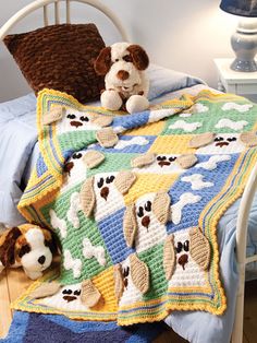 there is a crocheted afghan on the bed with two stuffed dogs sitting next to it