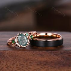 two wedding rings sitting on top of a wooden table next to each other with green stones