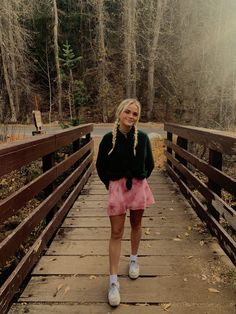 a woman standing on a wooden bridge in the woods