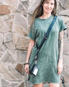 a woman standing in front of a stone wall with a camera strap around her neck