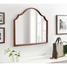 a mirror sitting on top of a white counter next to a bag and plant in a vase