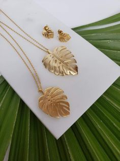 Gold plated monstera leaf necklaces + earrings. Necklace 1 is matte gold plated (brass), and necklace 2 is brushed gold plated (brass), and is slightly curved. The chains are both 18" long, with a 1.5" extender. The earrings are matte gold plated brass, and can have dangling 4mm bicone Swarovski crystals added in a variety of colors for no extra charge.  Gift wrapped. Gold Leaf Shaped Metal Jewelry, Gold Leaf Shaped Brass Jewelry, Gold Plated Leaf-shaped Jewelry, Handmade Gold Leaf-shaped Jewelry, Handmade Leaf-shaped Gold Jewelry, Leaf-shaped Yellow Gold Brass Jewelry, Gold Leaf-shaped Brass Jewelry, Leaf Necklaces, Jewellery Sets