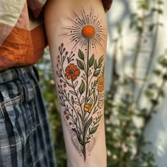 a woman's arm with flowers and sunbursts on it, in front of a bush