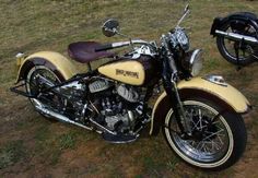 a yellow motorcycle parked on top of a grass covered field next to a black motorcycle