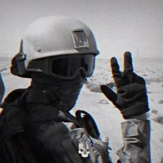 a man wearing a helmet and holding his hand up in the air while standing on top of snow covered ground