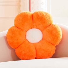 an orange flower shaped pillow sitting on top of a white chair