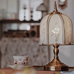 a glass lamp sitting on top of a table next to a cup and saucer