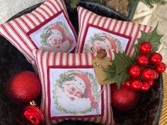 two christmas pillows with santa's face and holly on them, next to ornaments