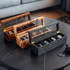 two wooden jewelry boxes sitting on top of a coffee table next to a couch with a watch in it