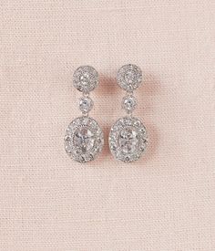 two pairs of diamond earrings sitting on top of a pink cloth