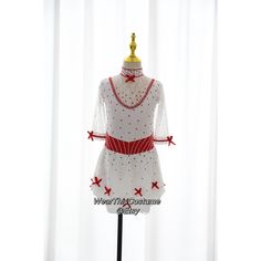 a white dress with red bows and pearls on the neckline is sitting on a mannequin