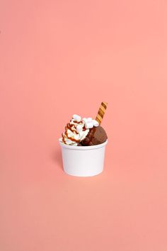 an ice cream sundae with chocolate and marshmallows in a white cup on a pink background