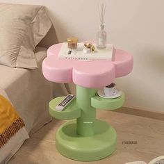 a pink and green side table on a wooden floor in front of a white bed