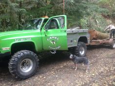 a green truck pulling a trailer with a dog in the bed and two men standing next to it