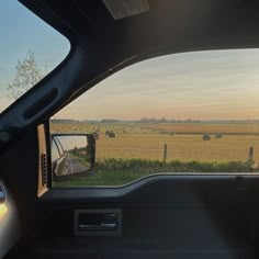 the rear view mirror of a car looking out at a field with hay bales