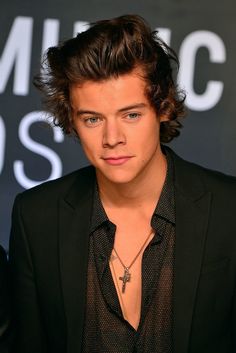 the young man is wearing a black suit and shirt with a cross necklace on his neck