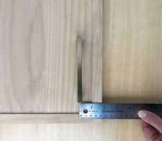 a person measuring the width of a cabinet door with a ruler on it's side