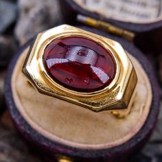 This bold ring features an East-to-West set oval cabochon garnet in a heavy 18k yellow gold mounting with a great patina and a European shank. The garnet has some surface dings and it is lightly cracked but the stone is stable and it is not noticeable when worn. The ring is currently a size 10 and can safely be resized between size 8.5 and 11.5. The ring is currently left unpolished. Luxury Ruby Ring With Oval Cabochon, Formal Yellow Gold Signet Ring With Oval Cabochon, Vintage Yellow Gold Gemstone Cabochons, Luxury Cabochon Signet Ring For Formal Occasions, Formal Yellow Gold Cabochons With Bezel Setting, Luxury Hallmarked Oval Cabochon Ruby Ring, Formal Cabochon Ruby Ring, Modernist Formal Cabochon Rings, Formal Cabochon Domed Ruby Ring