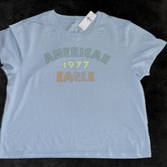 Nwt American Eagle Graphic Tee , Size Large. It’s A Baby Blue Color Retro Blue Tops With Letter Print, Retro Blue Top With Letter Print, Light Blue Graphic Tee With Letter Print, Retro Style Blue T-shirt For Spring, Blue Tops With Text Print For Spring, Blue Text Print Tops For Spring, Light Blue Basic Tops With Graphic Print, Light Blue Basic Top With Graphic Print, Basic Blue Tops With Graphic Print