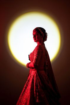 a woman standing in front of a bright light wearing a red dress and headpiece