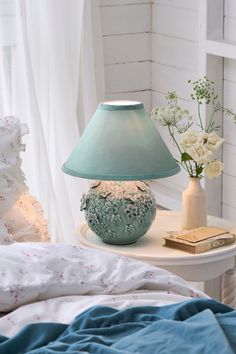 a blue lamp sitting on top of a white table next to a book and flowers