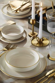 the table is set with gold and white plates, silverware, and candlesticks