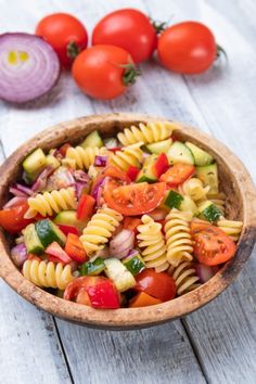 a wooden bowl filled with pasta salad next to tomatoes