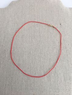 a red string is on top of a gray cloth with a gold beaded clasp