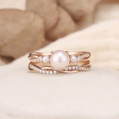 a pearl and diamond ring set on top of a white cushioned surface with rocks in the background