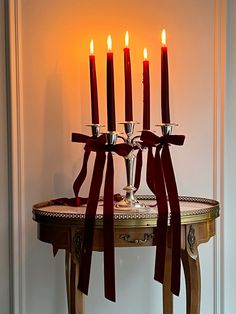 a table with candles on it in front of a white wall and red ribbon tied around the candle holders