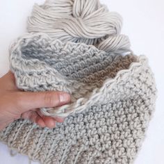 a hand is holding a gray and white crochet blanket with yarn on it