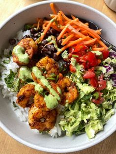 a bowl filled with shrimp, rice and veggies on top of a wooden table