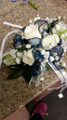 a bridal bouquet with white and blue flowers on a counter top next to a pair of pink shoes