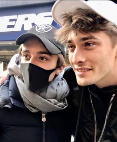 two people standing next to each other in front of a store wearing face coverings